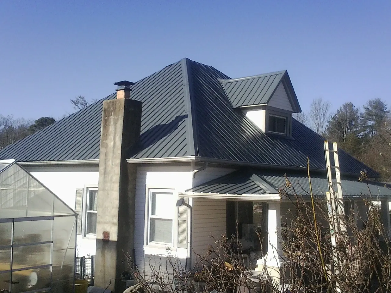 Dark blue standing seam metal roof on a white farmhouse with dormer — Slate & Tile Roof Repair by Roofing Brothers in Clark Fork