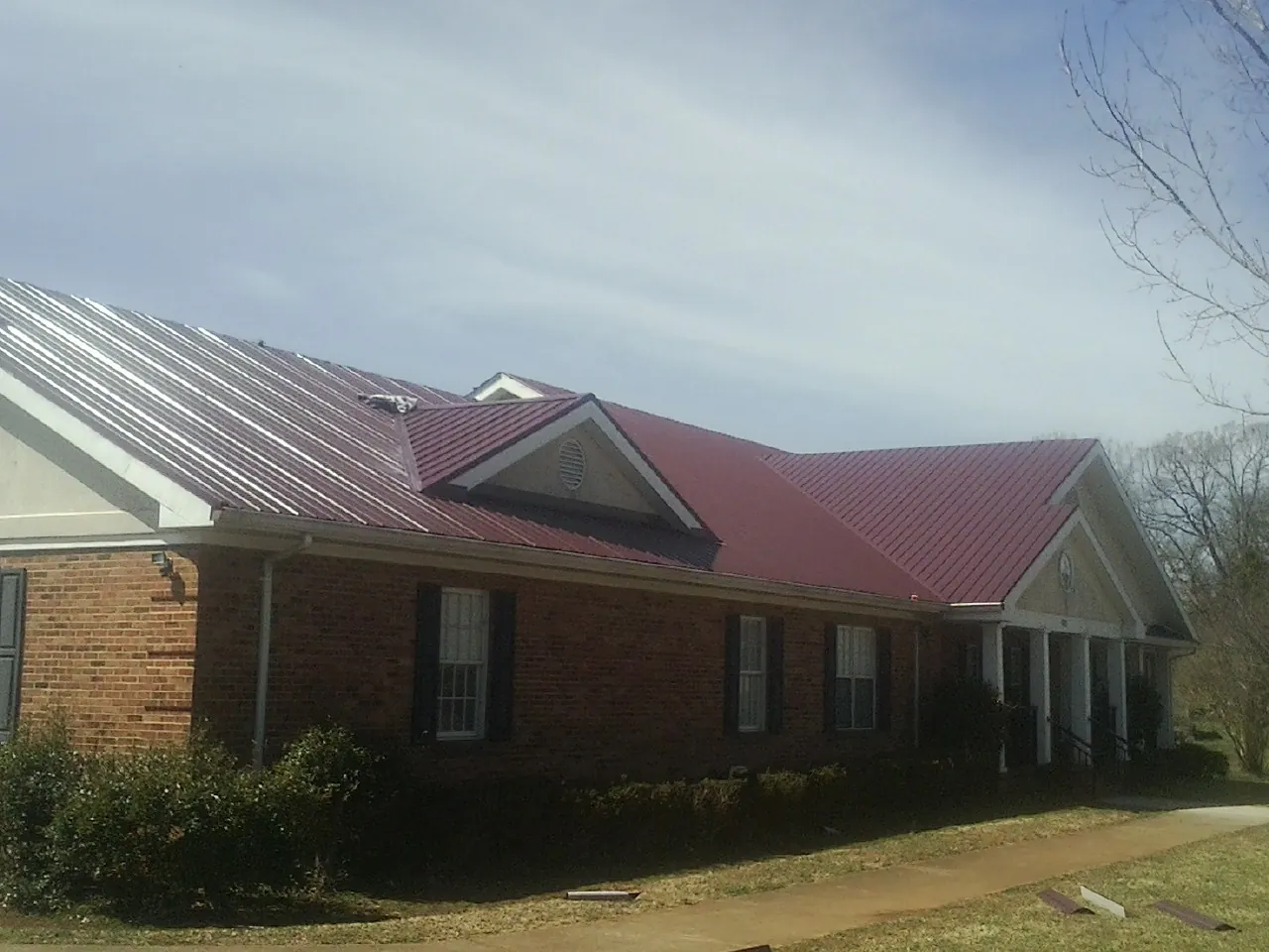 Red metal roof with gabled entries on a long brick building, from a Hail Damage Roof Repair job in Clark Fork