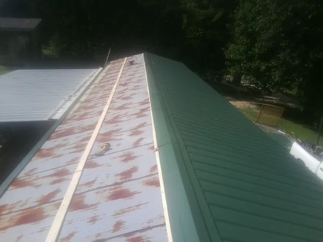 Old rusted panels beside newly installed green metal roofing — Wind Damage Roof Repair by Roofing Brothers in Clark Fork