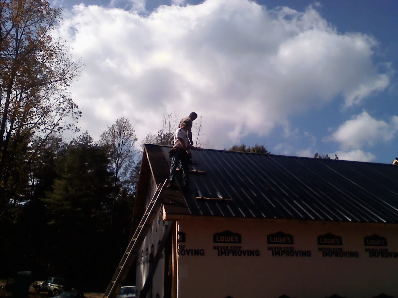 Roofer fastening dark metal panels high against a cloudy sky, from a Roof Inspection job in Clark Fork