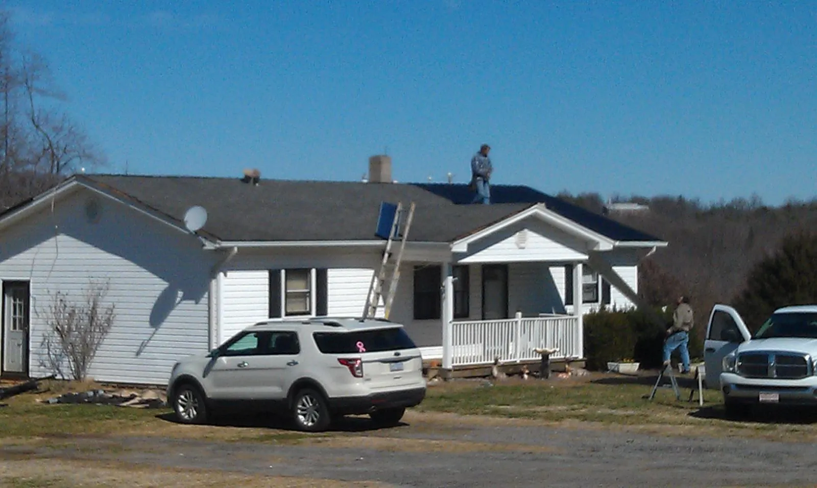 Roofers stripping shingles from a white ranch house roof in Clark Fork